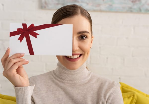 Beautiful girl covering face with gift card template and smiling at camera