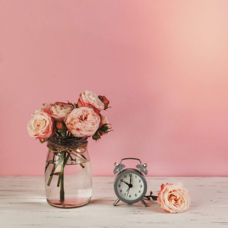 roses vase near alarm clock wooden desk against pink background