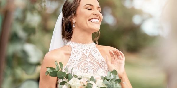 Excited bride in wedding with bouquet in nature park with green trees, bokeh and summer sunshine. Happiness, commitment and dream of a beauty woman with flowers for marriage in outdoor lens flare