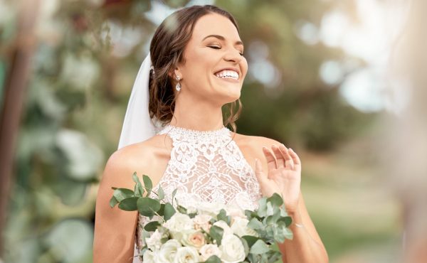 Excited bride in wedding with bouquet in nature park with green trees, bokeh and summer sunshine. Happiness, commitment and dream of a beauty woman with flowers for marriage in outdoor lens flare