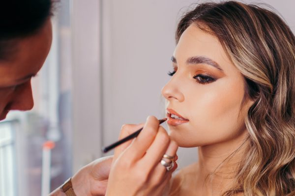 Female makeup artist applies rose lipstick. Beautiful females